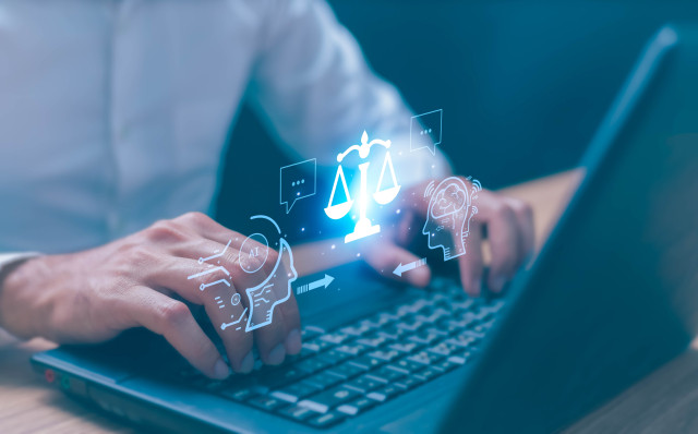 hands at laptop keyboard with holograph of justice balance.